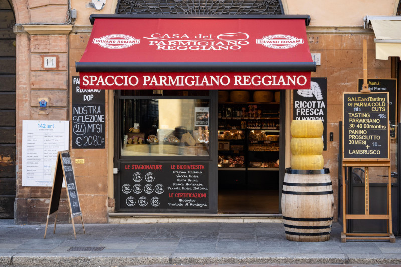 A traditional Italian delicatessen in Parma displays Parmigiano Reggiano wheels and offers authentic cheese tasting with local products.